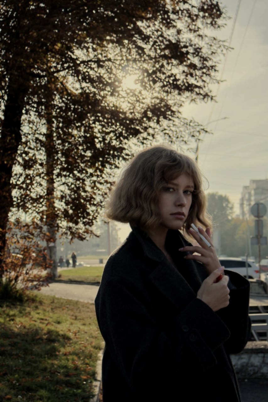 Between takes, a cigarette held near a collar, the coat shut, the bob unfixed